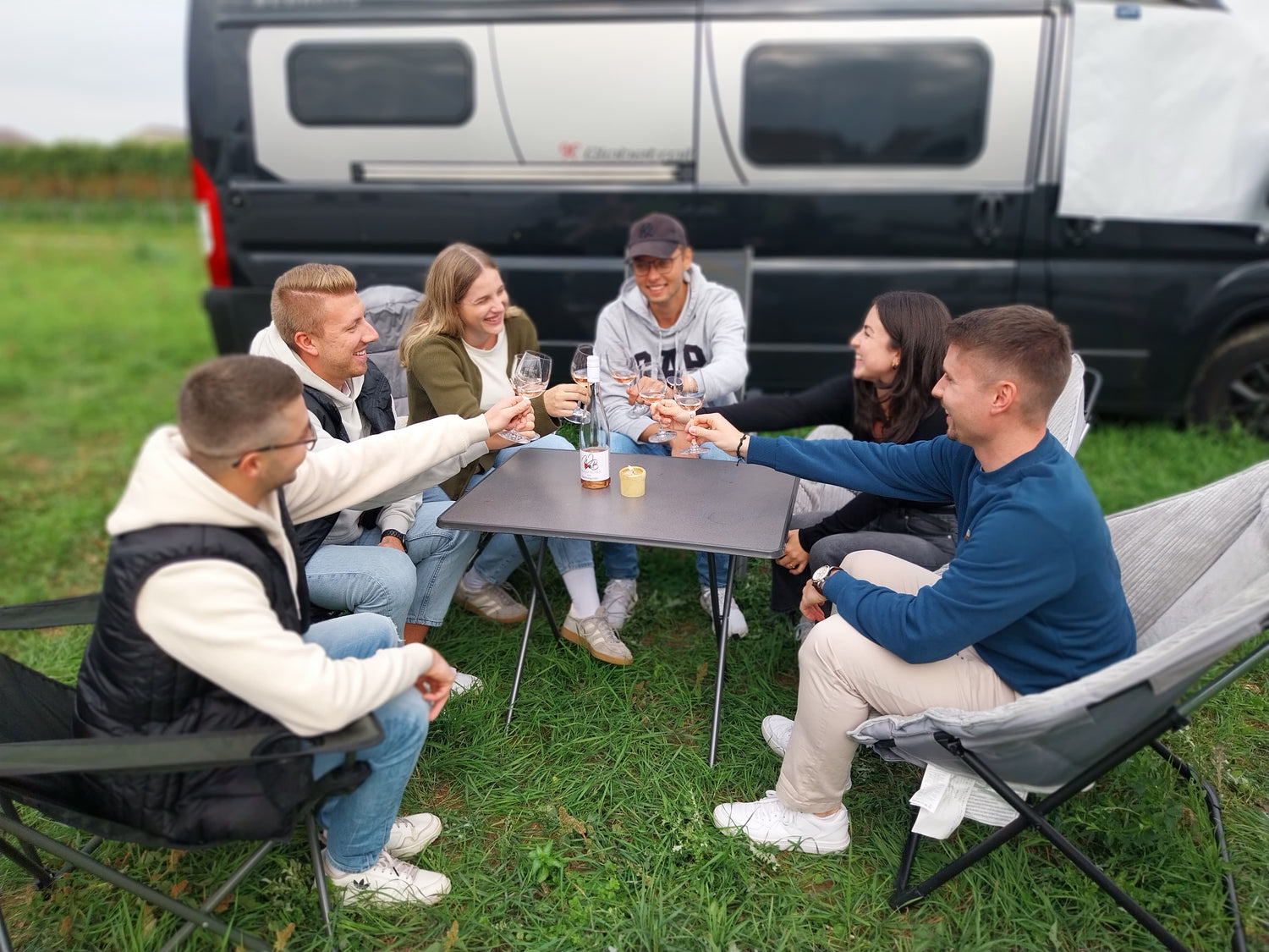 Gruppe auf Campingstühlen die gemeinsam mit Wein anstoßt